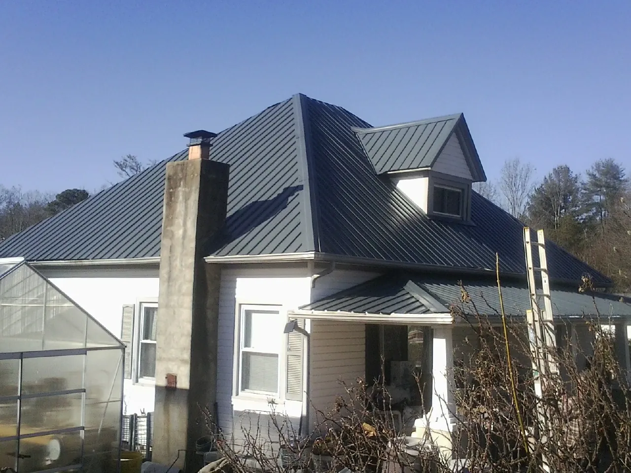 Dark blue standing seam metal roof on a white farmhouse with dormer — Slate & Tile Roof Repair by Roofing Brothers in Lakota