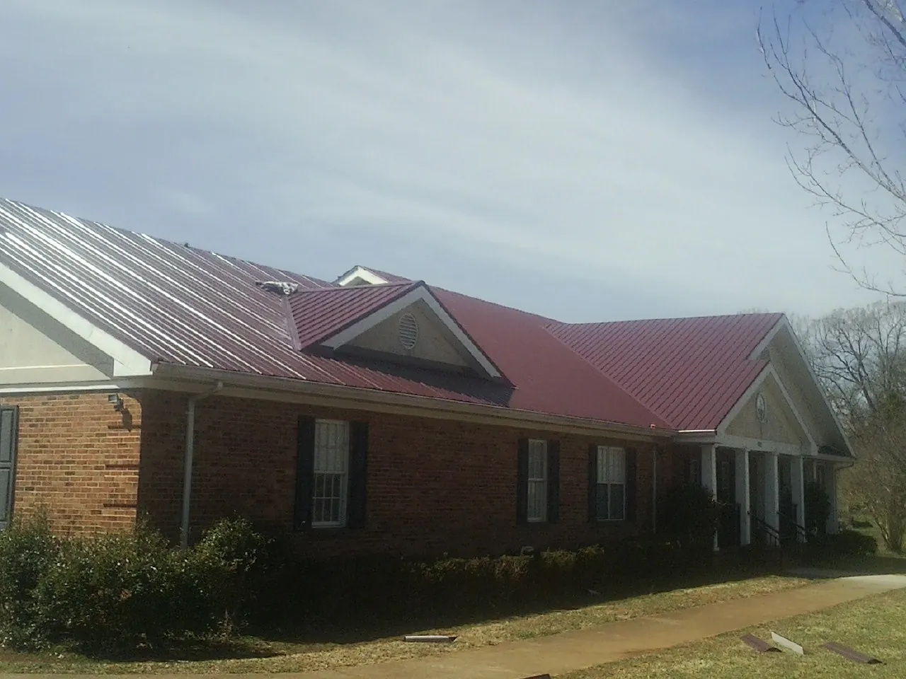 Red metal roof with gabled entries on a long brick building, from a Hail Damage Roof Repair job in Lakota