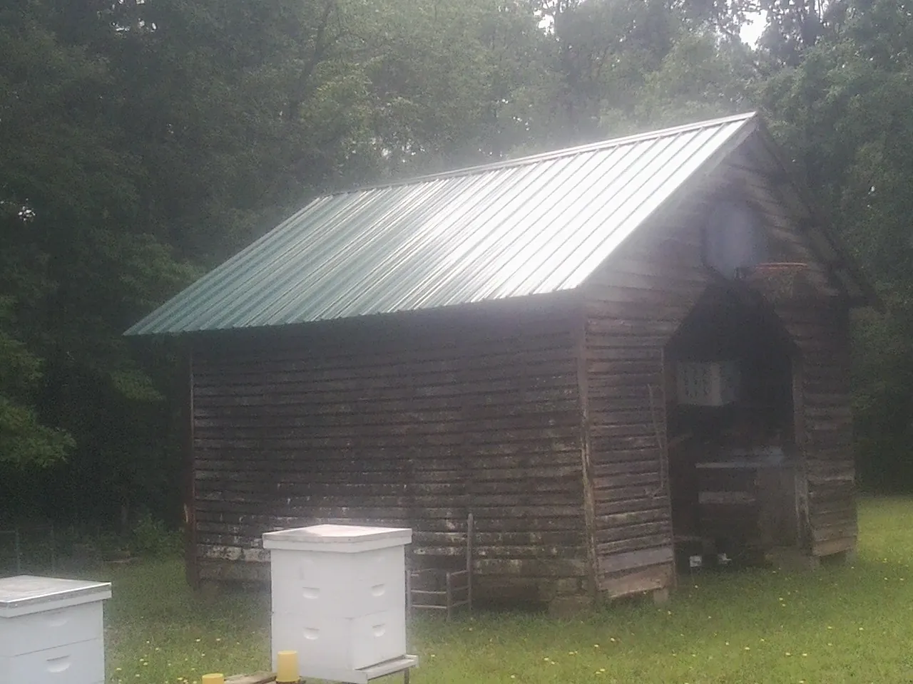 Green metal roof on a weathered barn beside stacked beehives in Lakota