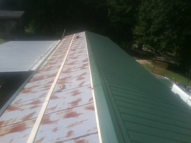 Old rusted panels beside newly installed green metal roofing — Wind Damage Roof Repair by Roofing Brothers in Lakota