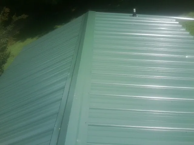 New green metal panels meeting at the ridge of a roof — Flat Roof Repair work by our crew in Lakota
