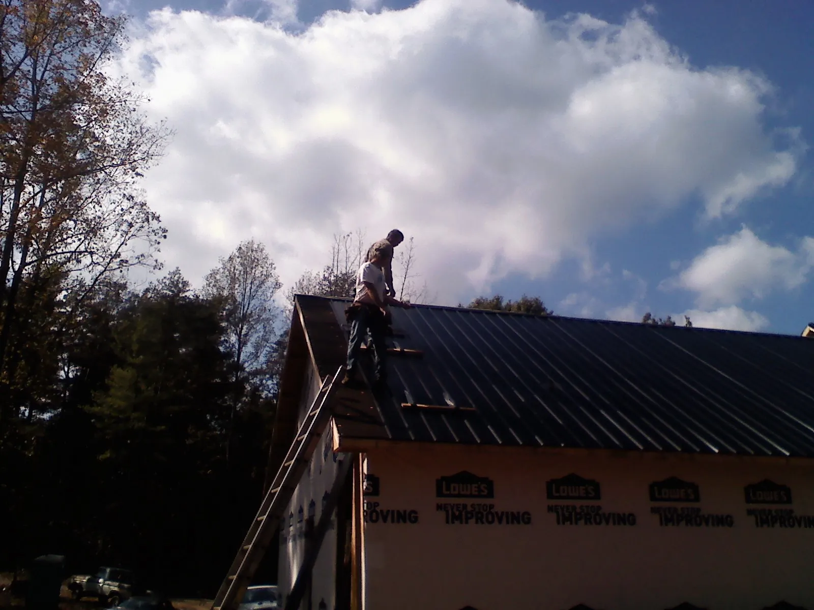 Roofer fastening dark metal panels high against a cloudy sky, from a Roof Inspection job in Lakota