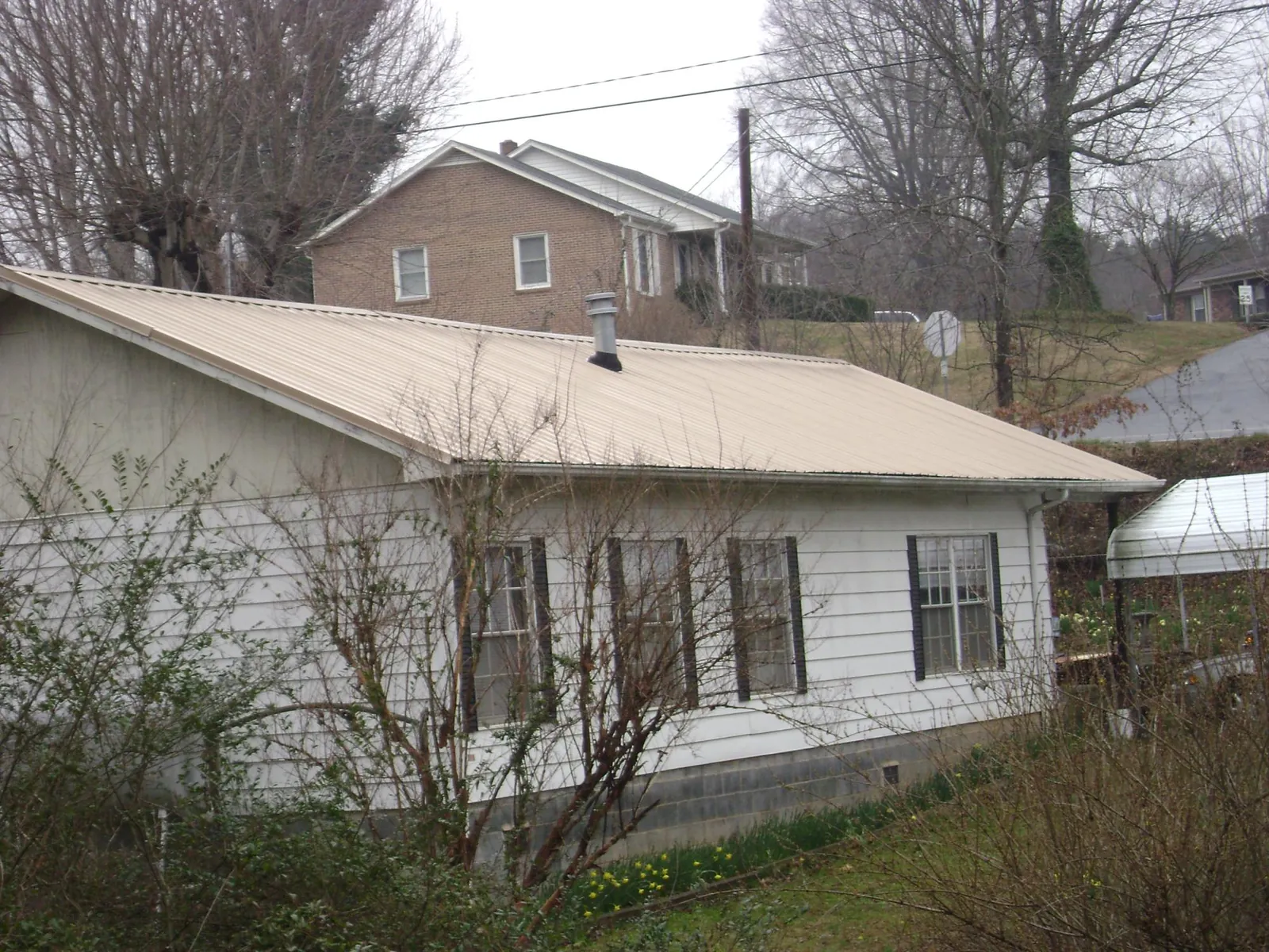 Tan metal roof on a white sided house set into a hillside — Commercial Roofing by Roofing Brothers in Lakota