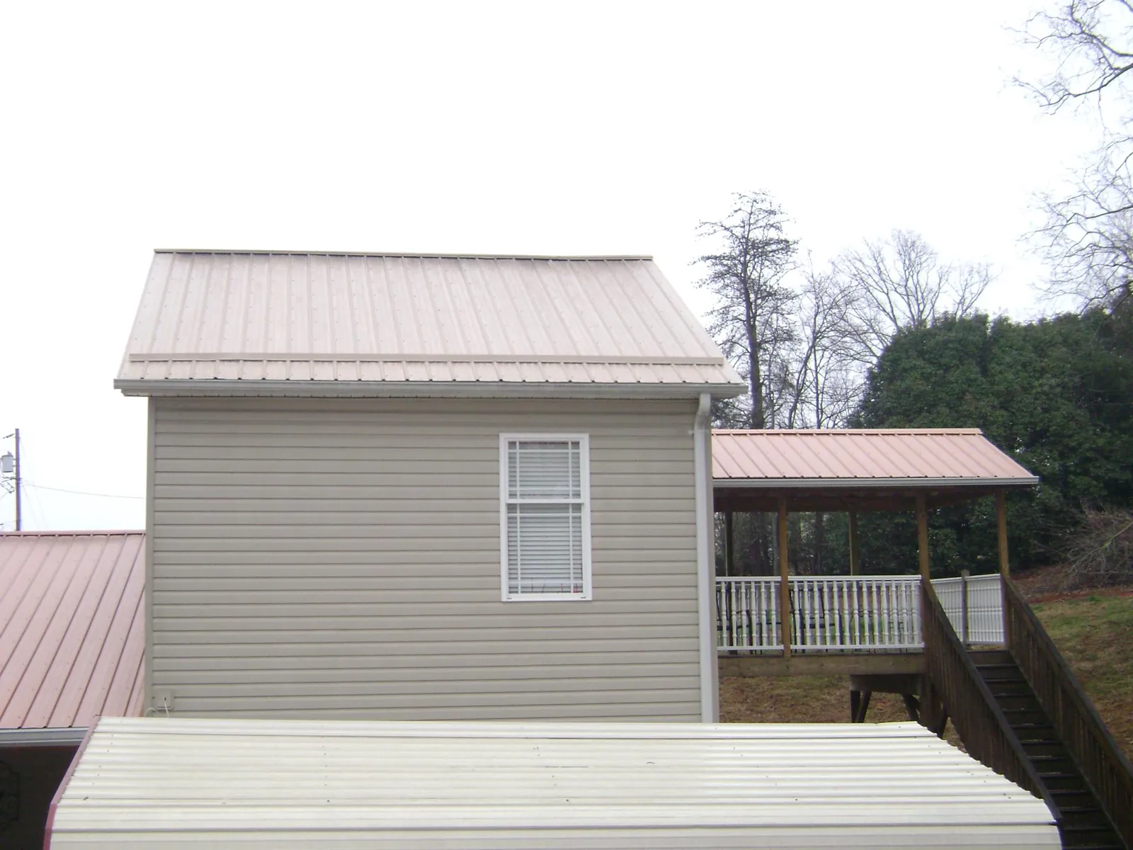 Tan metal roofs on a two story addition and attached porch, from a Roof Replacement job in Lakota